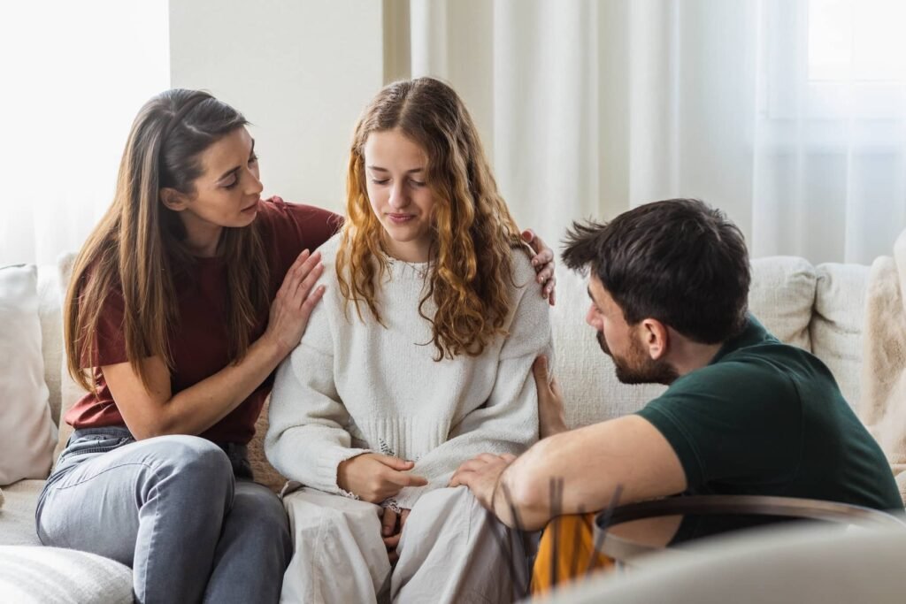 Parents comforting and talking with their teenage daughter during a family discussion at home, representing compassionate communication, emotional support, and professional family therapy for parenting and family issues.