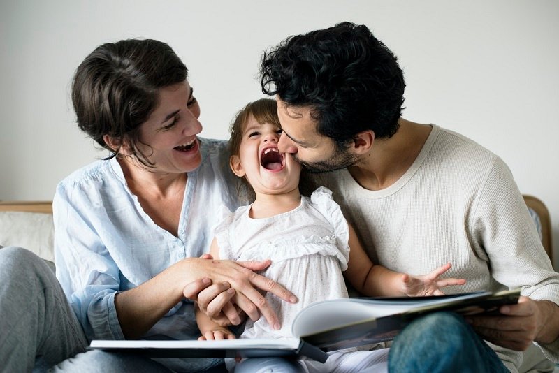 Parents reading a book and laughing with their young daughter at home, representing parenting support therapy and healthy family relationships in San Francisco.