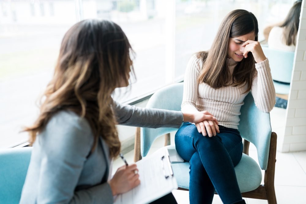 A therapist comforting an emotional client during a counseling session in a brightly lit office.